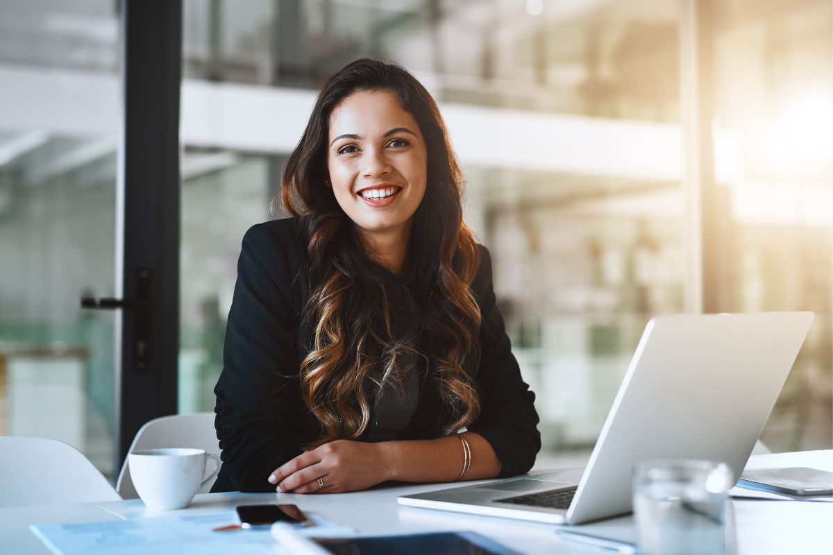 photo of a woman in front of a laptop sitting at a desk and smiling